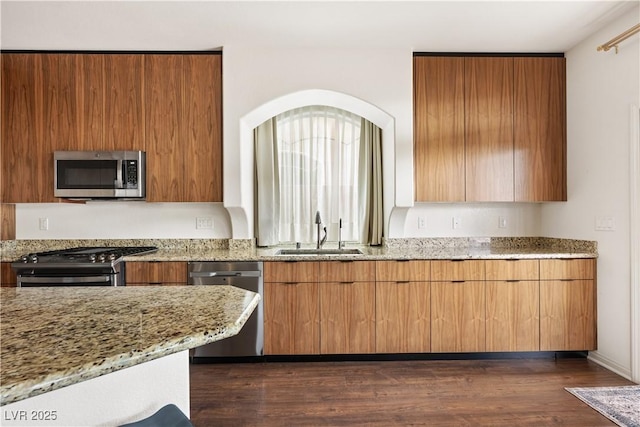 kitchen featuring modern cabinets, light stone countertops, a sink, dark wood-style floors, and stainless steel appliances