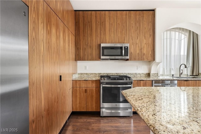 kitchen featuring a sink, appliances with stainless steel finishes, brown cabinetry, and light stone counters