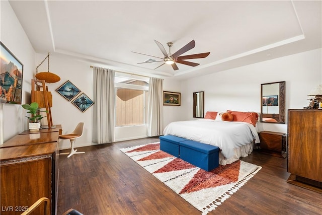 bedroom with baseboards, ceiling fan, wood finished floors, and a raised ceiling