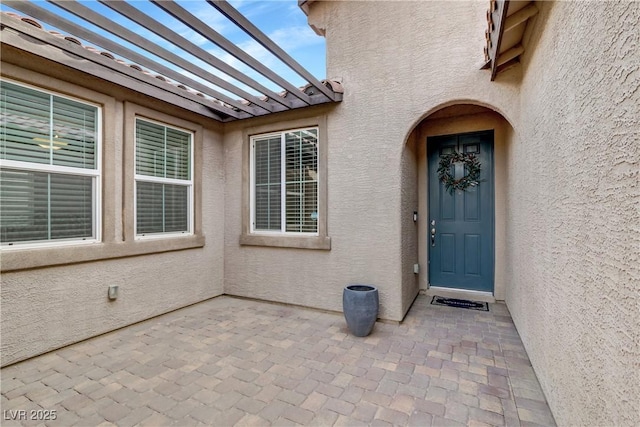 entrance to property with a patio area, stucco siding, and a pergola