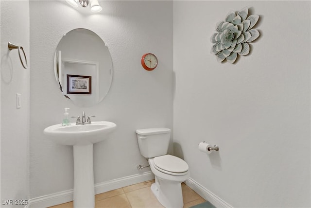 half bathroom with baseboards, toilet, tile patterned floors, and a sink