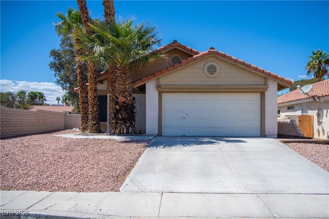 mediterranean / spanish home featuring an attached garage, stucco siding, a tiled roof, and fence