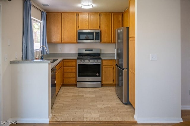 kitchen featuring appliances with stainless steel finishes, light wood-type flooring, a sink, baseboards, and light countertops