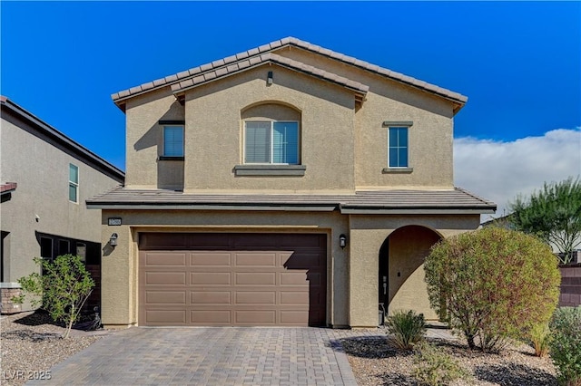 mediterranean / spanish-style home featuring an attached garage, decorative driveway, stucco siding, and a tiled roof