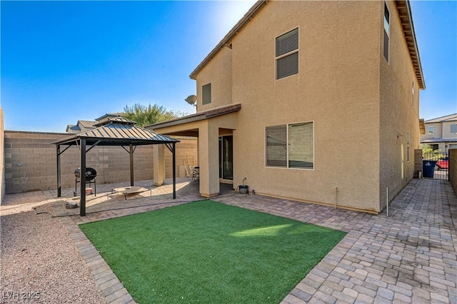 back of house with a lawn, fence private yard, a gazebo, a patio, and stucco siding
