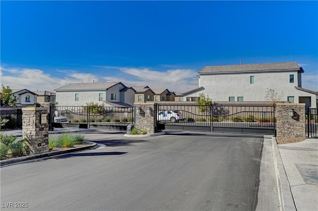 view of street with a gate, a gated entry, curbs, and a residential view