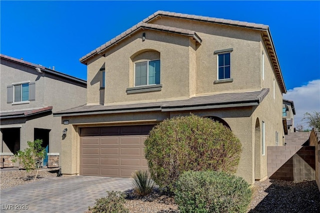 traditional home with a tiled roof, stucco siding, an attached garage, and decorative driveway
