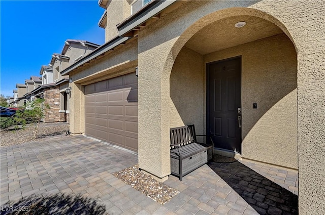 view of exterior entry featuring stucco siding, an attached garage, and driveway