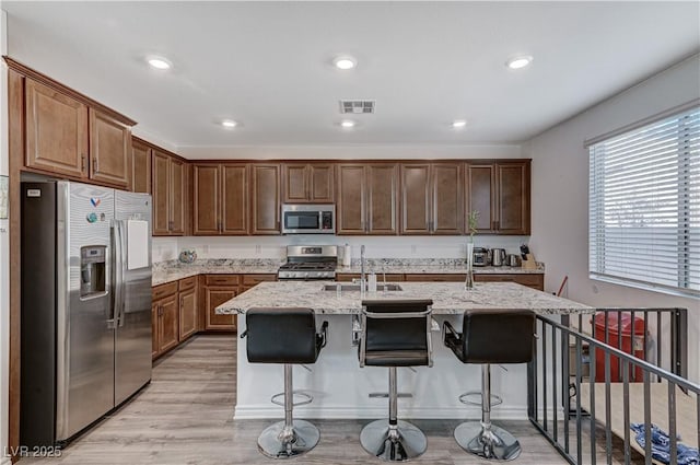 kitchen with light stone countertops, appliances with stainless steel finishes, a sink, light wood-type flooring, and visible vents