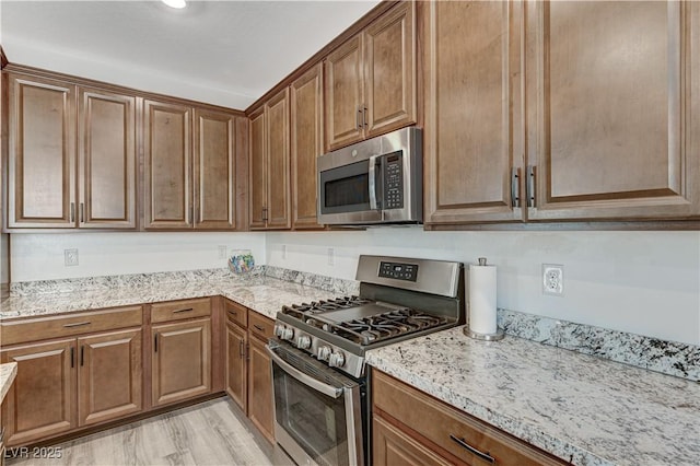 kitchen with brown cabinetry, light wood-style flooring, light stone countertops, and stainless steel appliances
