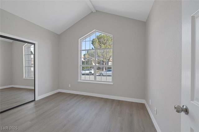 unfurnished bedroom featuring baseboards, lofted ceiling with beams, and wood finished floors