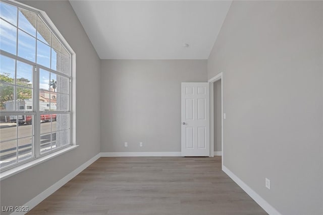 unfurnished room with baseboards, vaulted ceiling, and wood finished floors