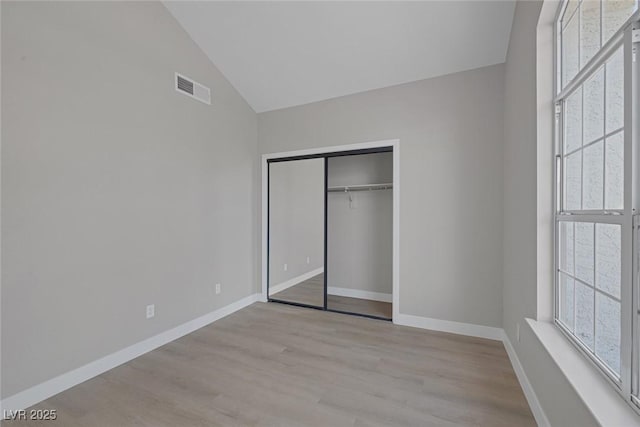 unfurnished bedroom with visible vents, wood finished floors, baseboards, a closet, and lofted ceiling