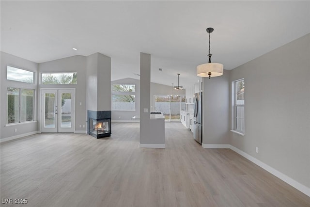 unfurnished living room featuring baseboards, a multi sided fireplace, lofted ceiling, and light wood-type flooring