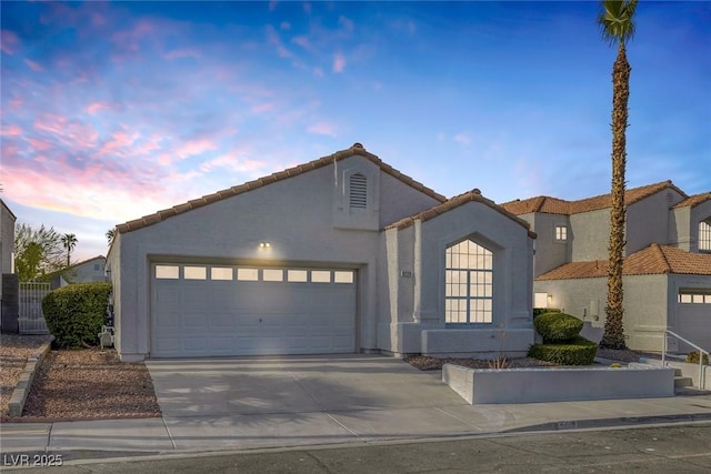view of front of home with a garage, stucco siding, driveway, and a tiled roof