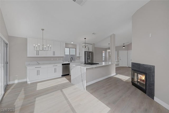 kitchen featuring baseboards, white cabinetry, light wood finished floors, a premium fireplace, and stainless steel appliances