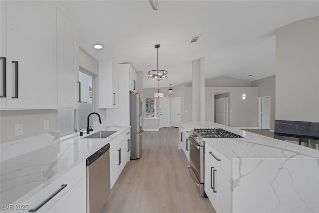 kitchen with a sink, stainless steel appliances, white cabinetry, light wood-type flooring, and vaulted ceiling