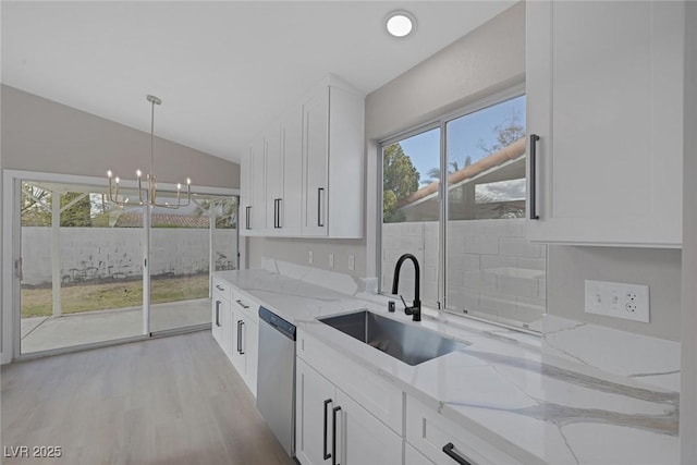 kitchen with lofted ceiling, light stone counters, a sink, dishwasher, and a notable chandelier