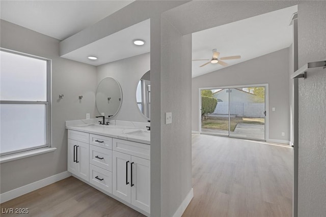 full bathroom featuring double vanity, ceiling fan, vaulted ceiling, wood finished floors, and baseboards