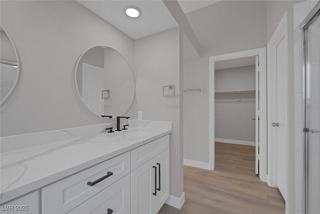 bathroom featuring a walk in closet, a shower stall, wood finished floors, vanity, and baseboards
