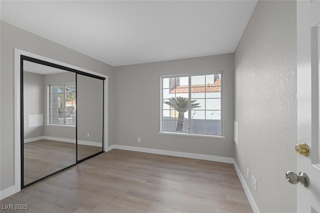 unfurnished bedroom featuring baseboards, a textured wall, a closet, and wood finished floors