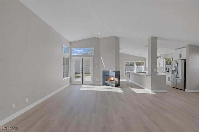 unfurnished living room featuring baseboards, a sink, vaulted ceiling, and light wood-type flooring