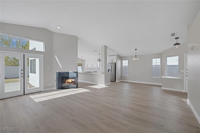 unfurnished living room with baseboards, light wood-style flooring, visible vents, and high vaulted ceiling