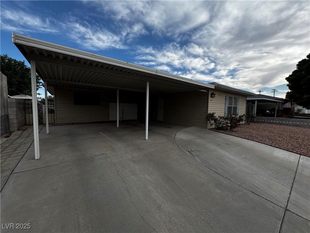 view of vehicle parking with driveway, fence, and an attached carport