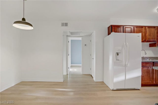 kitchen with white refrigerator with ice dispenser, light wood finished floors, and visible vents