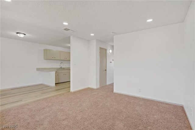unfurnished living room with a textured ceiling, baseboards, visible vents, and light carpet