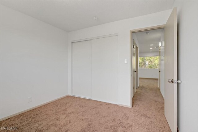 unfurnished bedroom featuring baseboards, light carpet, and a closet