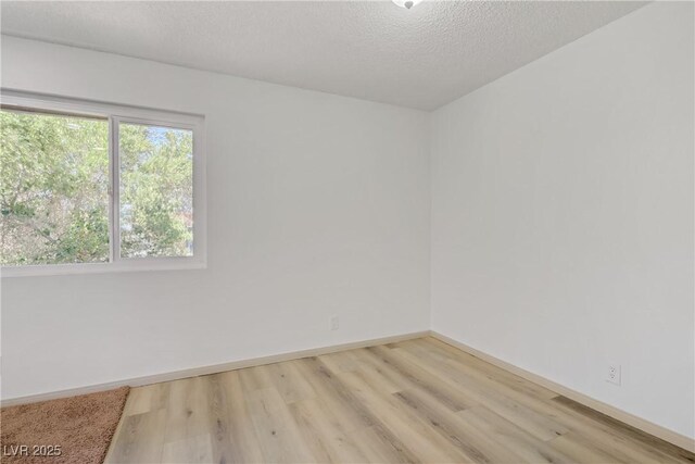 spare room with a textured ceiling, baseboards, and light wood finished floors