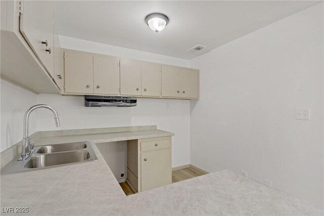 kitchen featuring light wood-type flooring, a sink, cream cabinetry, and light countertops