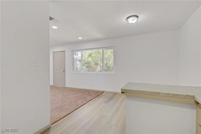spare room featuring a textured ceiling, visible vents, baseboards, recessed lighting, and light wood-style flooring