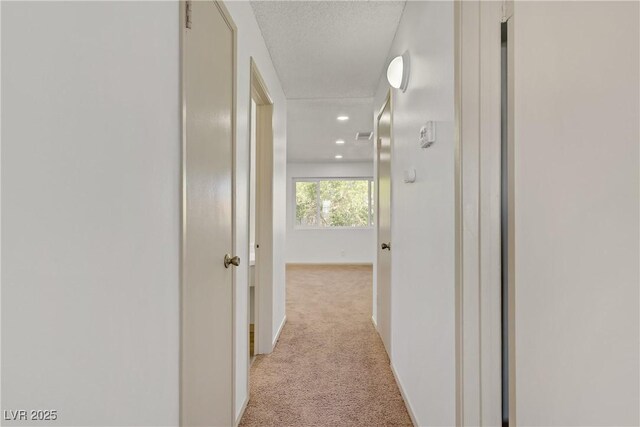 corridor featuring recessed lighting, baseboards, light colored carpet, and a textured ceiling