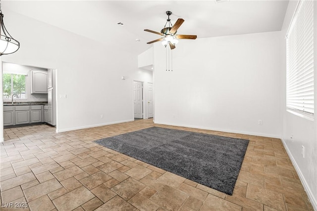 unfurnished living room with baseboards, ceiling fan, high vaulted ceiling, a sink, and stone finish flooring