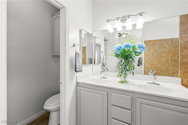 bathroom with a sink, baseboards, toilet, and double vanity