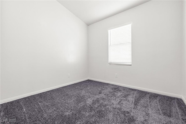 empty room with baseboards, vaulted ceiling, and dark colored carpet