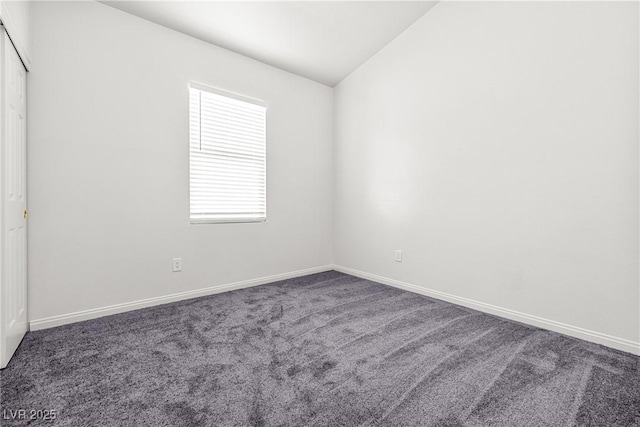 carpeted empty room featuring baseboards and vaulted ceiling