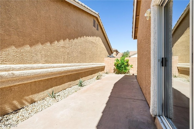 view of side of home with stucco siding, a patio area, and fence
