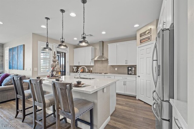 kitchen featuring wall chimney range hood, appliances with stainless steel finishes, a sink, recessed lighting, and a kitchen bar