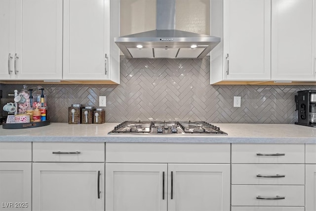 kitchen featuring wall chimney exhaust hood, stainless steel gas cooktop, backsplash, and white cabinetry