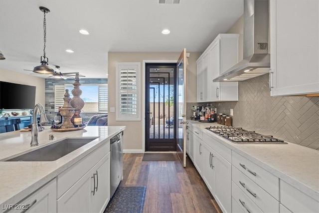 kitchen with decorative backsplash, ceiling fan, wall chimney range hood, a sink, and appliances with stainless steel finishes