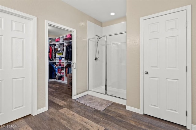 bathroom with a shower stall, wood finished floors, baseboards, a spacious closet, and recessed lighting