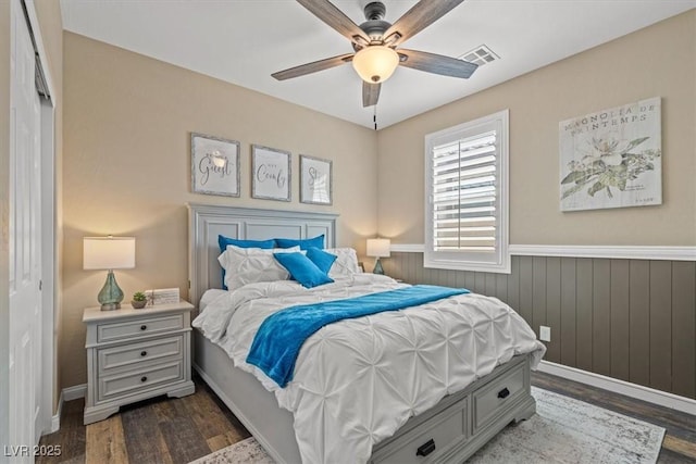 bedroom with visible vents, dark wood finished floors, ceiling fan, and a wainscoted wall
