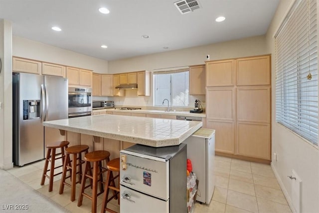 kitchen featuring appliances with stainless steel finishes, light brown cabinets, light countertops, a kitchen island, and visible vents