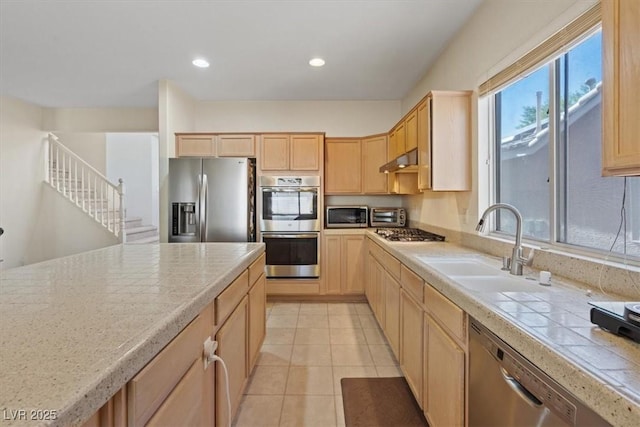kitchen featuring a sink, under cabinet range hood, light brown cabinets, stainless steel appliances, and light tile patterned flooring