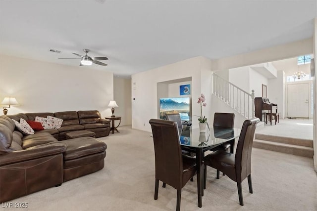 dining area with stairs, light colored carpet, visible vents, and ceiling fan with notable chandelier