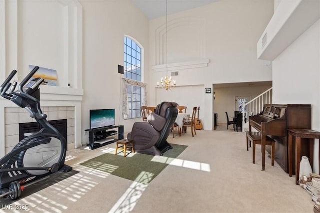 living area featuring carpet floors, a towering ceiling, stairway, a tiled fireplace, and a notable chandelier
