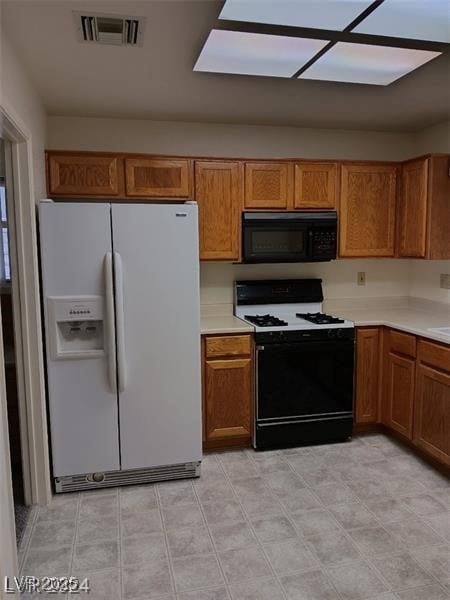 kitchen featuring visible vents, black microwave, white refrigerator with ice dispenser, gas range, and brown cabinets